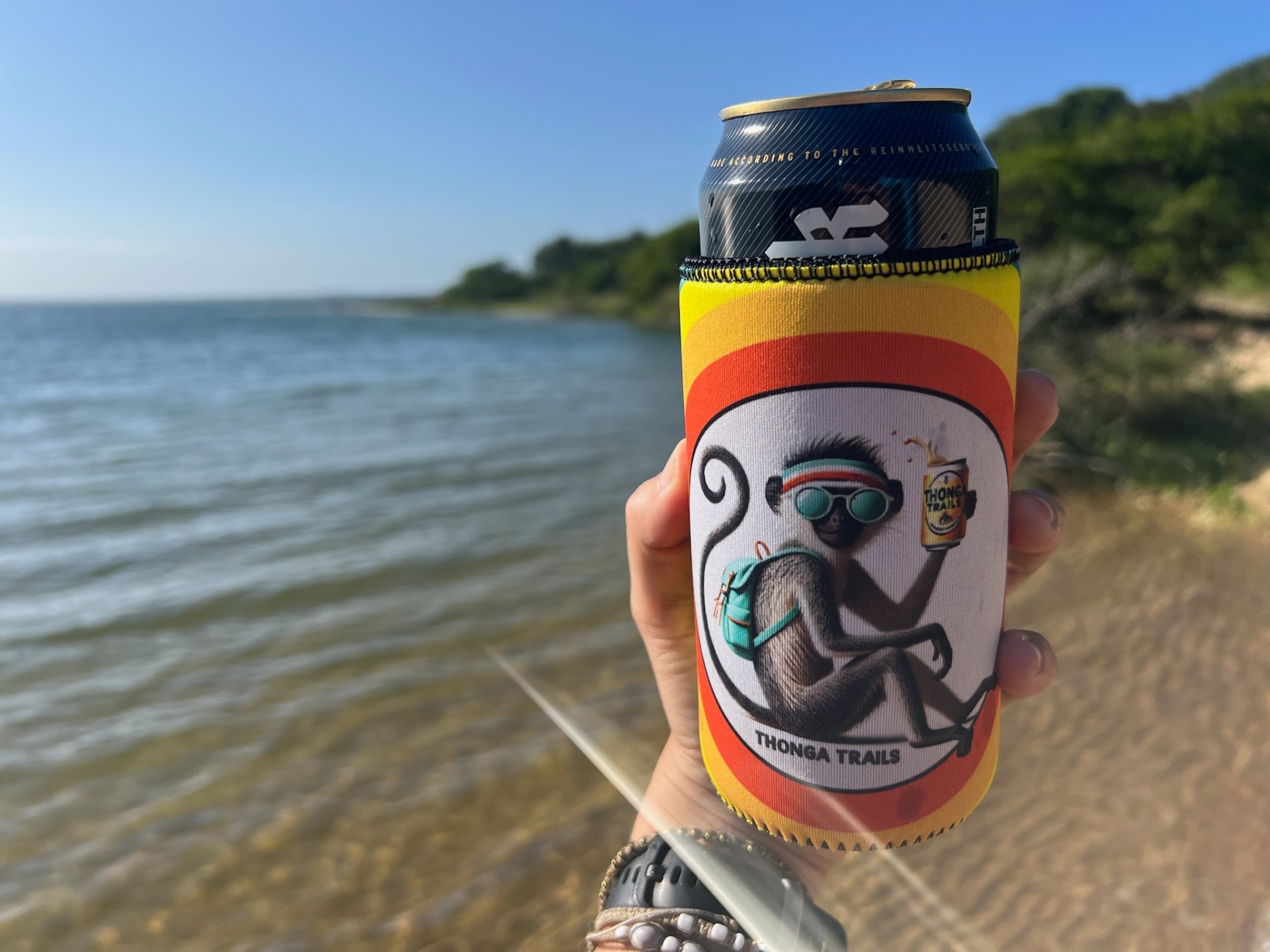 Thonga Trails koozie holding a cold beer by the lake